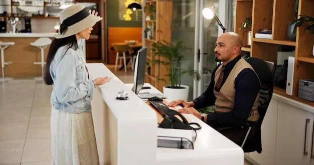 A front desk agent smiling and engaging in conversation with a hotel guest, a check-in counter in the background.