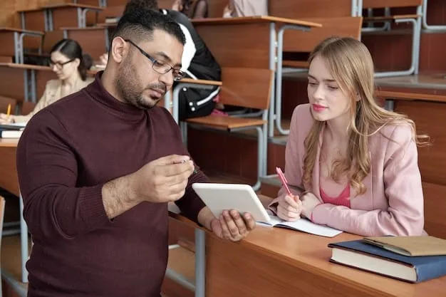 An experienced female teacher gently guiding a younger male teacher through a lesson plan on a tablet, with diverse students blurred in the background, illustrating mentorship and collaborative learning.