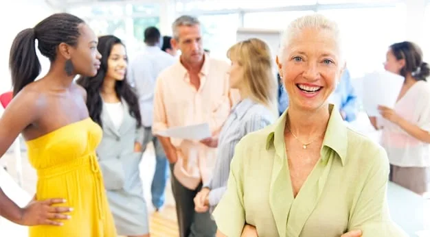 A diverse group of people, appearing to be in their 30s to 50s, gathered around a table with a financial advisor, looking at screens and documents related to retirement planning. They are engaged in discussion, suggesting collective strategizing for future financial security.