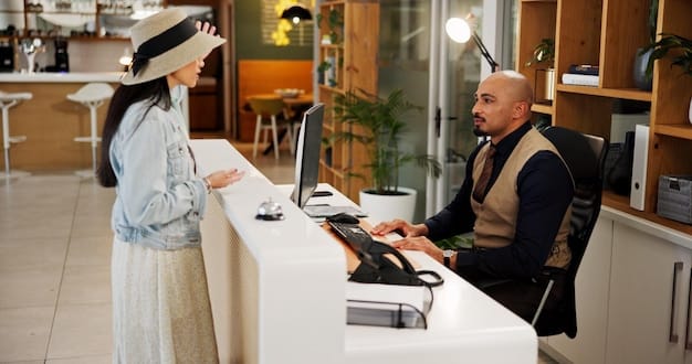 A front desk agent smiling and engaging in conversation with a hotel guest, a check-in counter in the background.