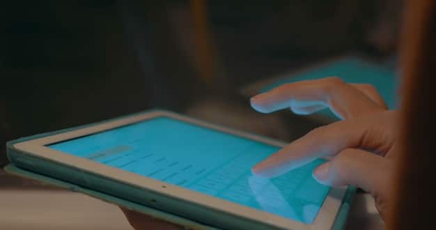 A close-up of a hand pointing to a digital compliance checklist on a tablet, with various software icons representing data management and security in the background.
