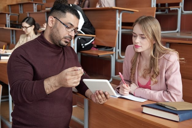 An experienced female teacher gently guiding a younger male teacher through a lesson plan on a tablet, with diverse students blurred in the background, illustrating mentorship and collaborative learning.